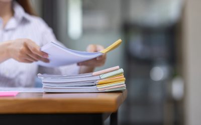 Person ordnet bunte Dokumente auf Schreibtisch.